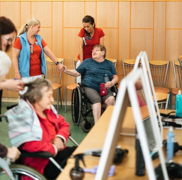 Caregivers interacting warmly with elderly women in wheelchairs in a community care setting